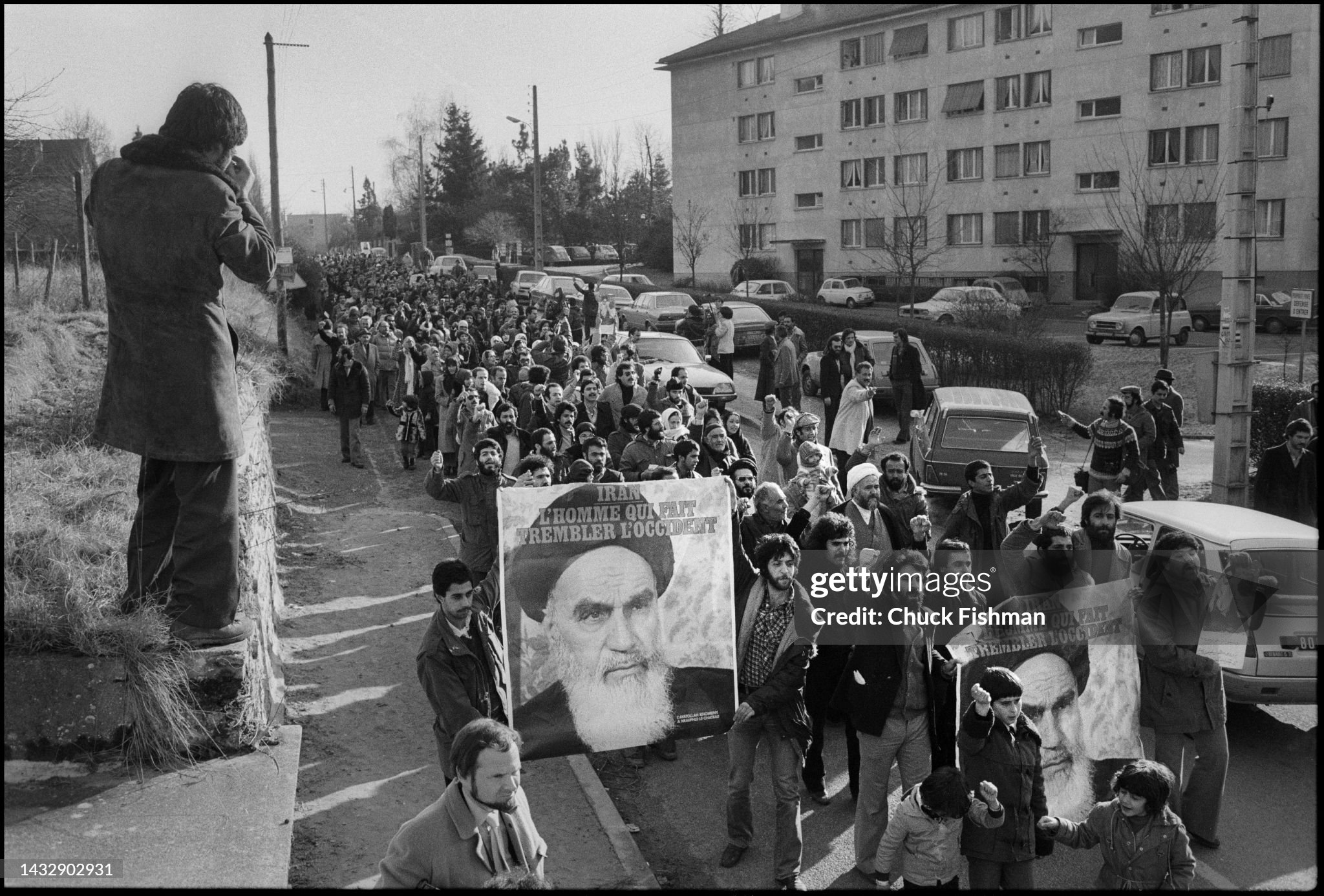 法国人支持霍梅尼的示威游行&nbsp;1979年1月，在法国诺夫勒堡，有人站在墙头拍摄支持霍梅尼的示威游行队伍沿路行进的画面。当时，霍梅尼在流亡生涯中居住在该镇。（图片来源：Chuck Fishman） 